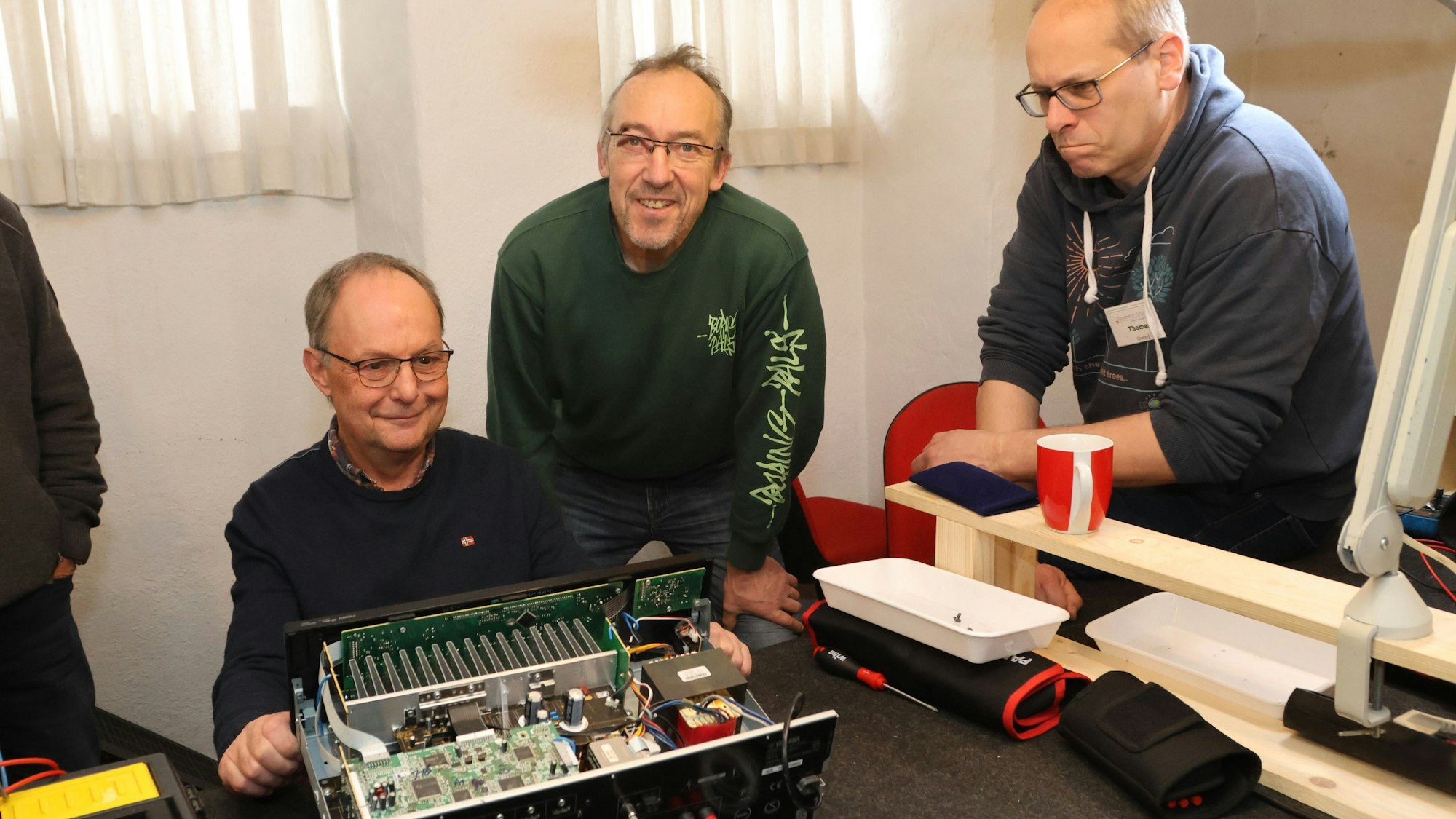 Der Ehrenamtler Diethelm Noll (links), repariert den Verstärker des Waldbrölers Martin Klein (Mitte) im Waldbröler Repair-Café, ein weiterer Helfer gibt Tipps von der Seite.