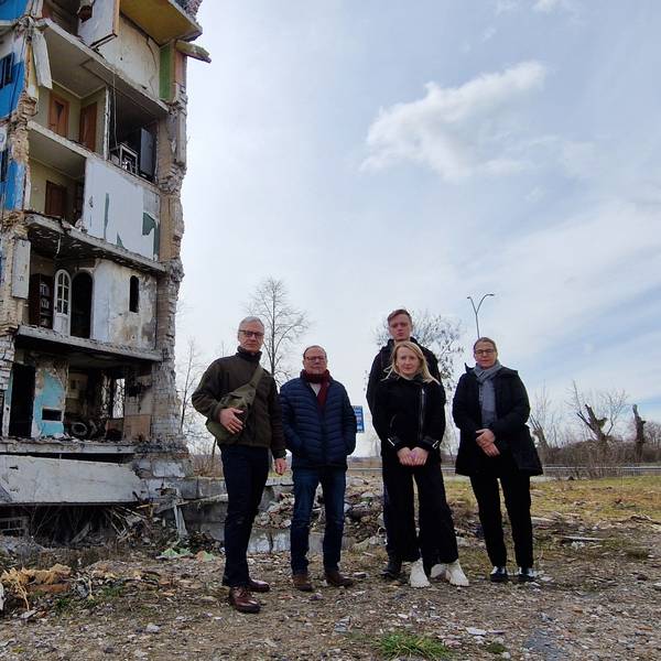 Das Foto zeigt ein Gruppenbild vor einem schwer beschädigten Wohnblock.