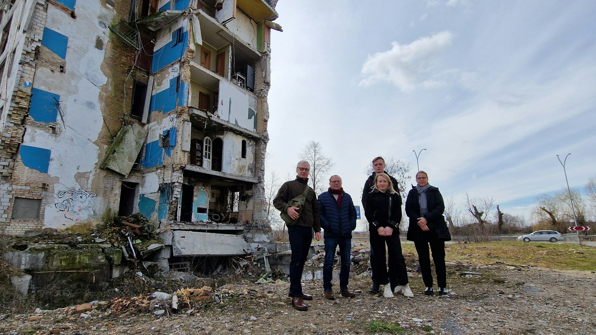 Das Foto zeigt ein Gruppenbild vor einem schwer beschädigten Wohnblock.