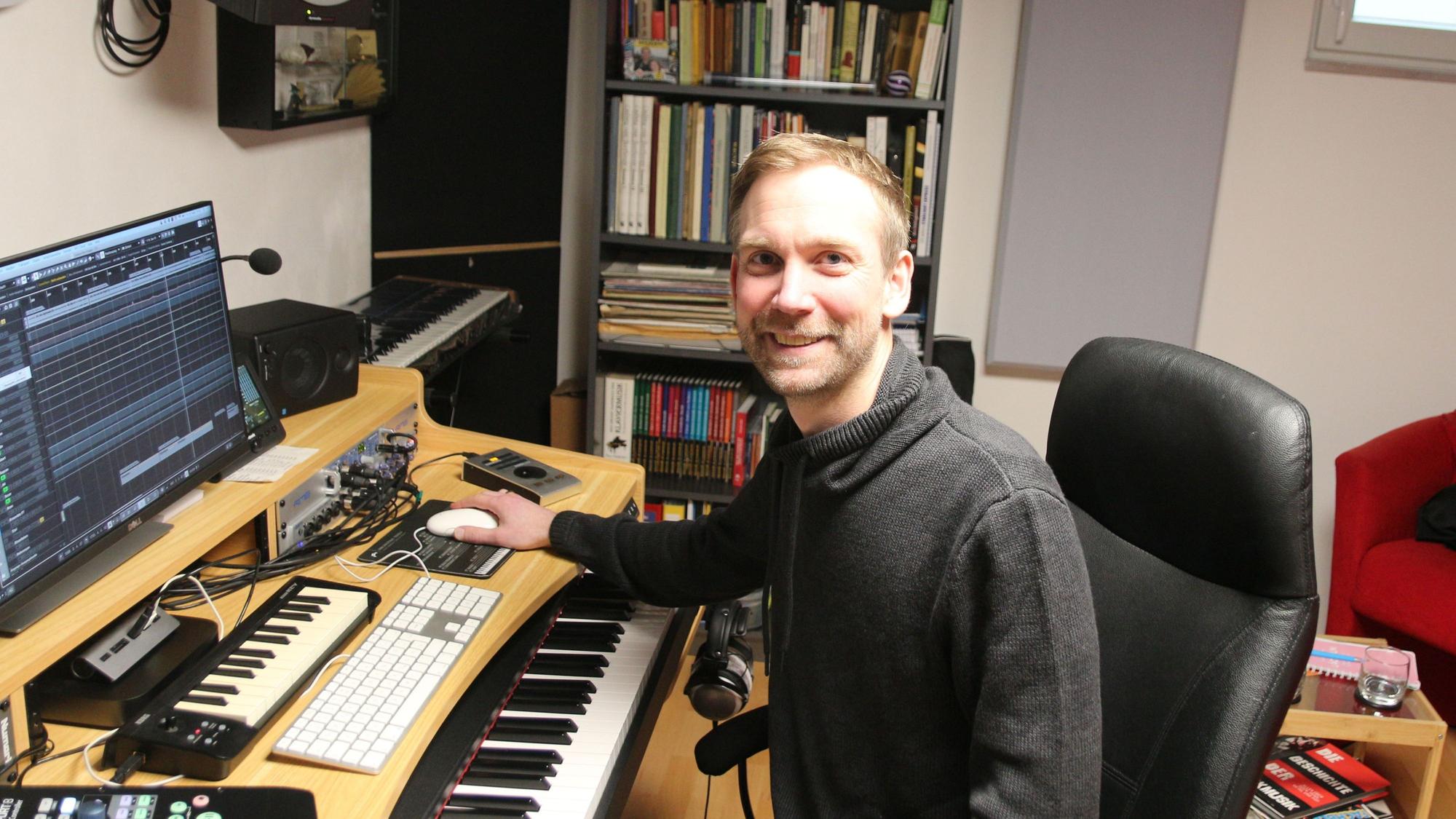 Der Musiker sitzt in seinem Tonstudio und lächelt in die Kamera.