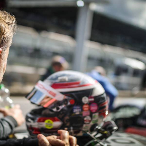 Ein Rennfahrer schaut am Nürburgring in Richtung Boxengasse, im Hintergrund ein Helm.