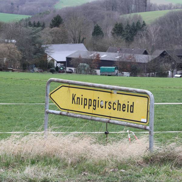 Blick über ein landwirtschaftliche Wiese auf ein Gehöft mit einem Schild im Vordergrund, das den Weg zum Dorf Knippgierscheid zeigt.