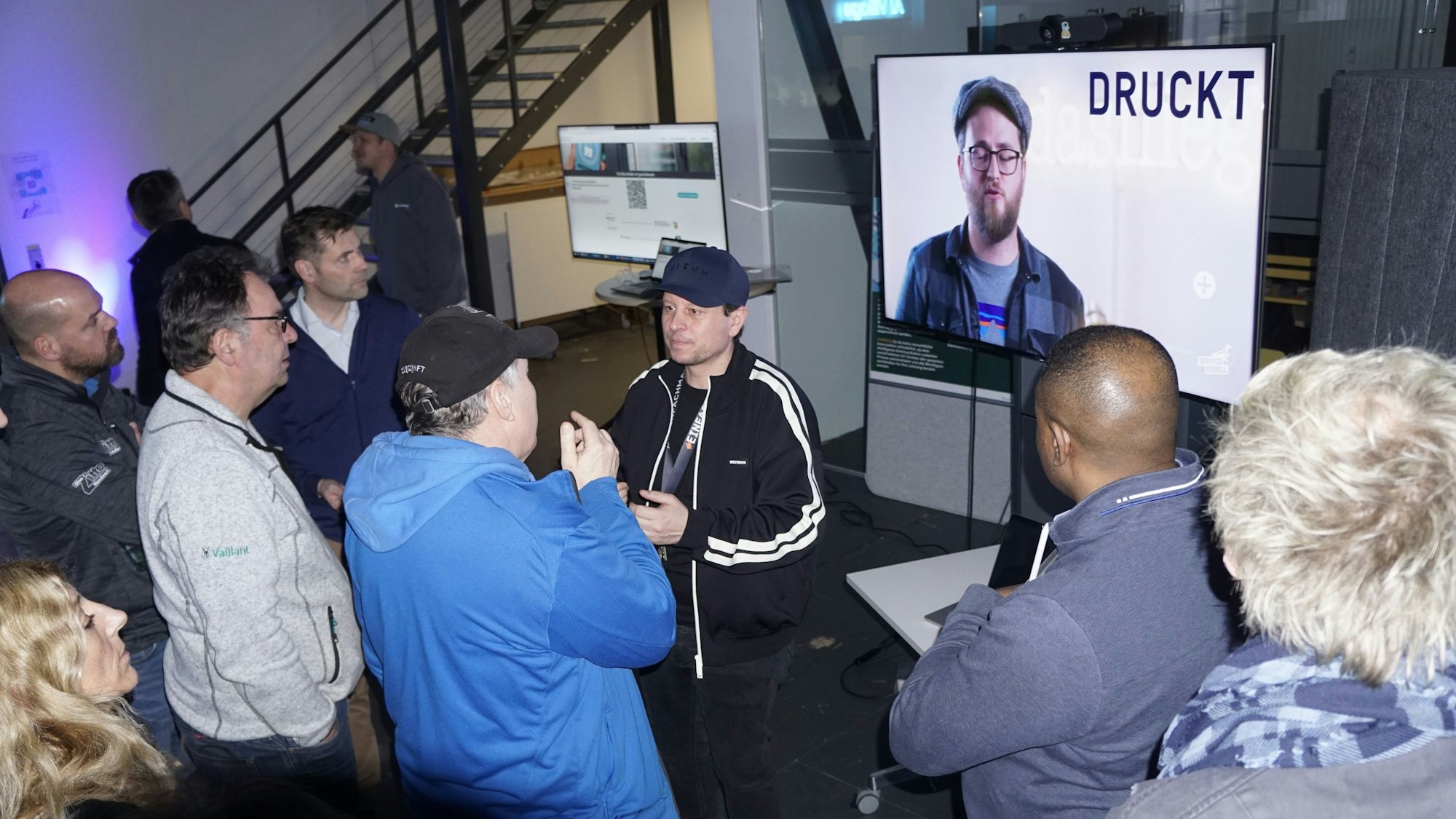 Vertreter von Handwerksbetrieben stehen vor einem großen Bildschirm im AI Village und diskutieren mit einem Experten.