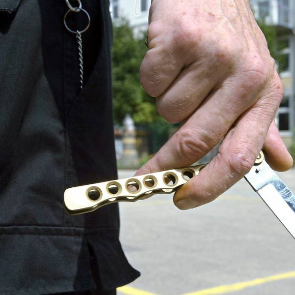 Ein Mann hält auf dem Hof einer Schule ein sogenanntes Butterflymesser in seiner Hand.