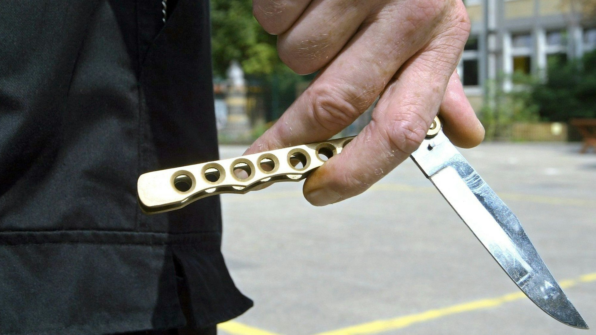 Ein Mann hält auf dem Hof einer Schule ein sogenanntes Butterflymesser in seiner Hand.