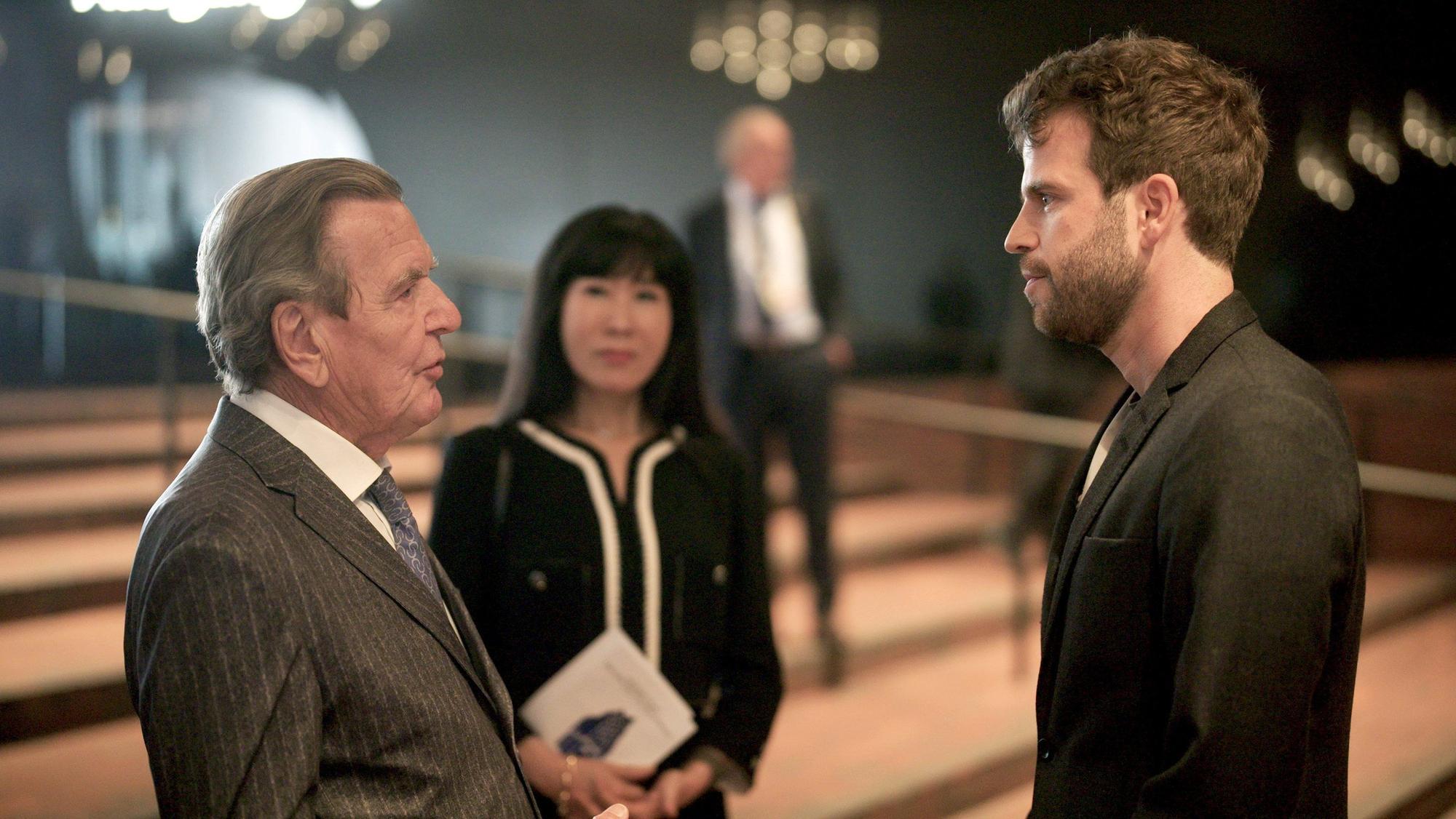 Lucas Stratmann, Gerhard Schröder und Soyeon Schröder-Kim stehen auf einer Treppe in der Elbphilharmonie.