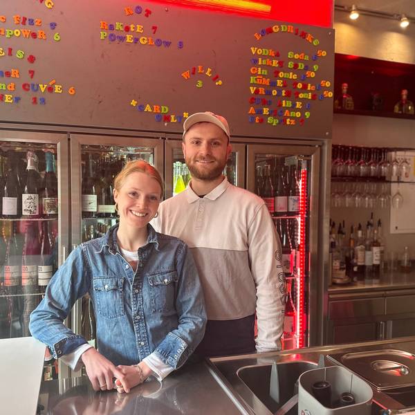 Ein junger Mann und eine junge Frau stehen hinter einer Bar und lächeln