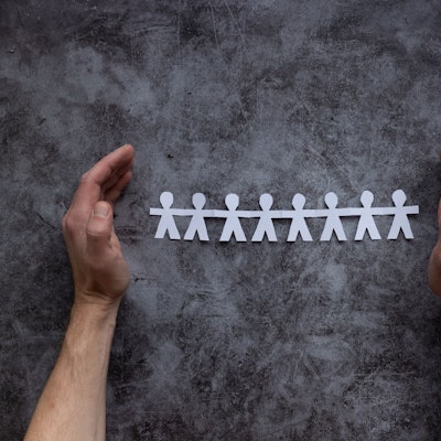 Zwei Hände schützen ausgeschnittene Papiermännchen