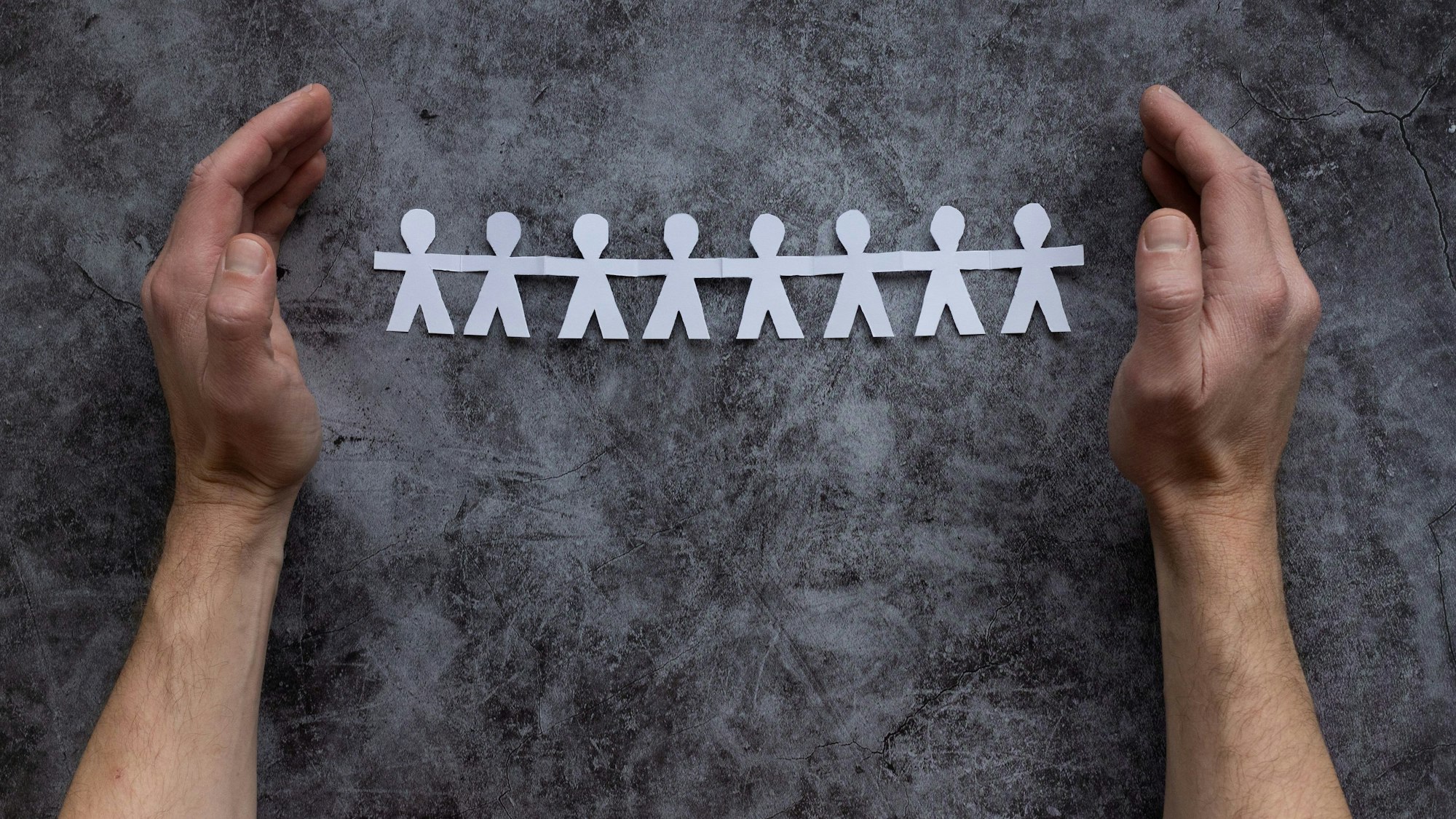 Zwei Hände schützen ausgeschnittene Papiermännchen