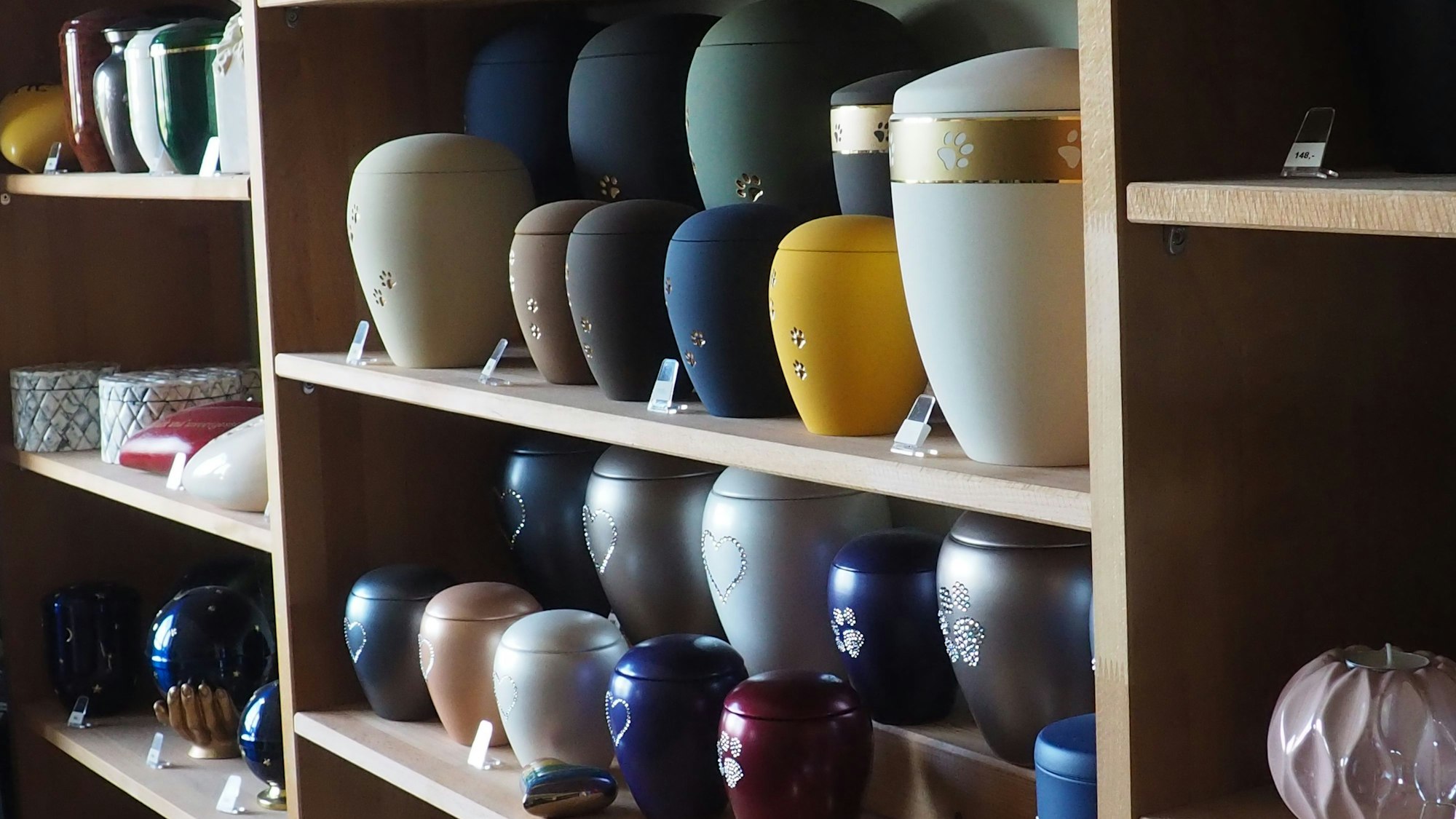 Zu sehen sind unterschiedliche Urnen für die Asche von Tieren in einem Regal.