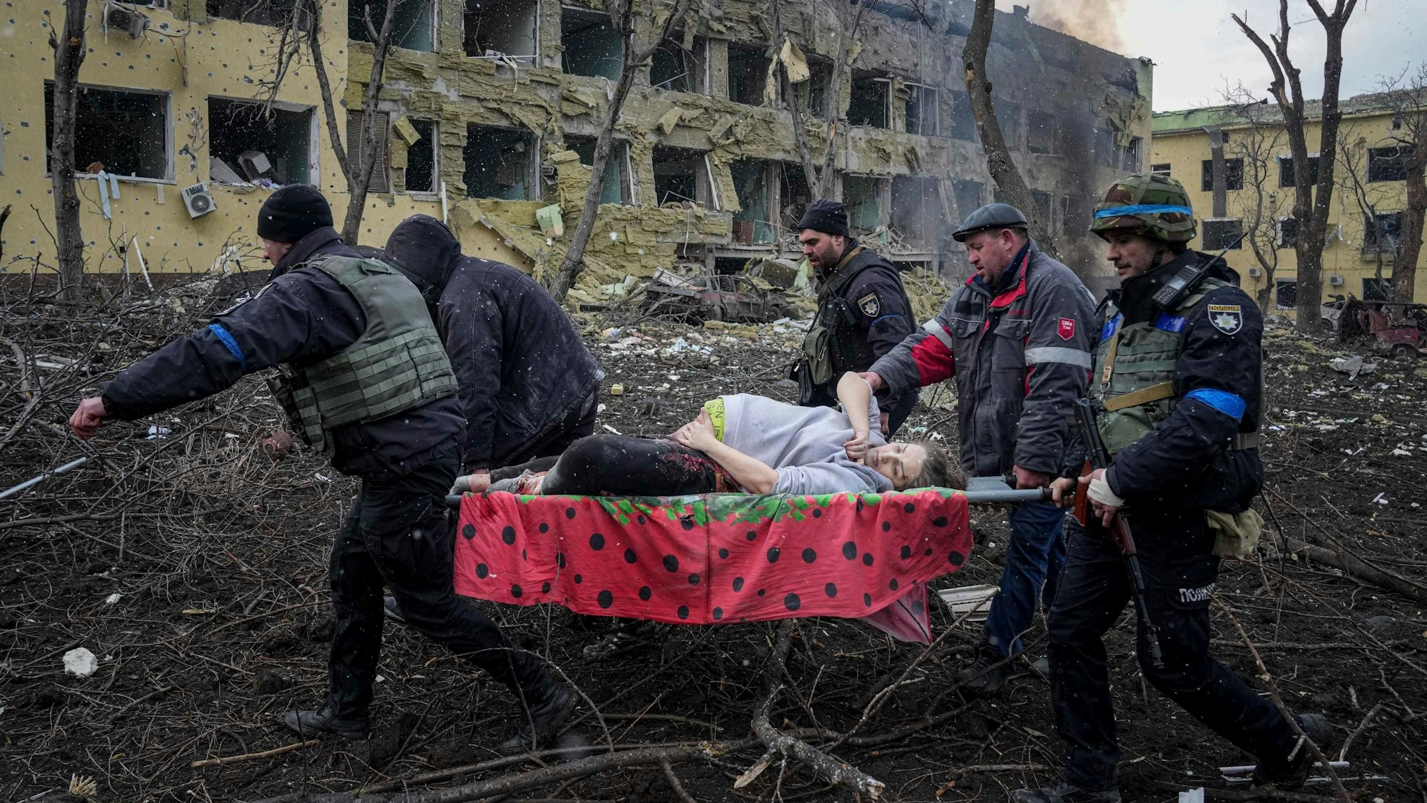 Ukrainische Rettungskräfte und Freiwillige tragen eine verletzte schwangere Frau aus einer Entbindungsklinik, die im März 2023 durch russischen Beschuss beschädigt wurde.