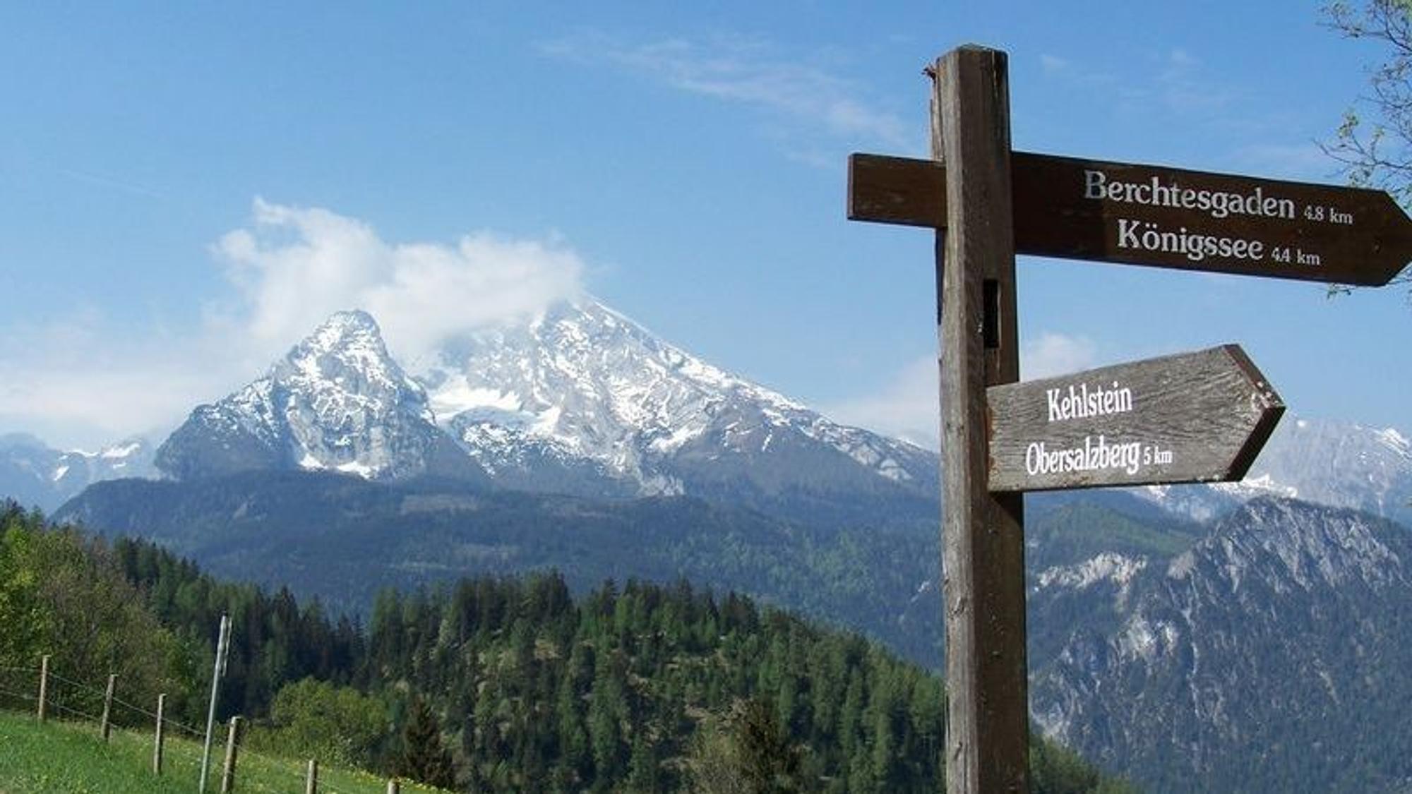 Ein Wegweiser steht vor den Berchtesgadener Alpen.