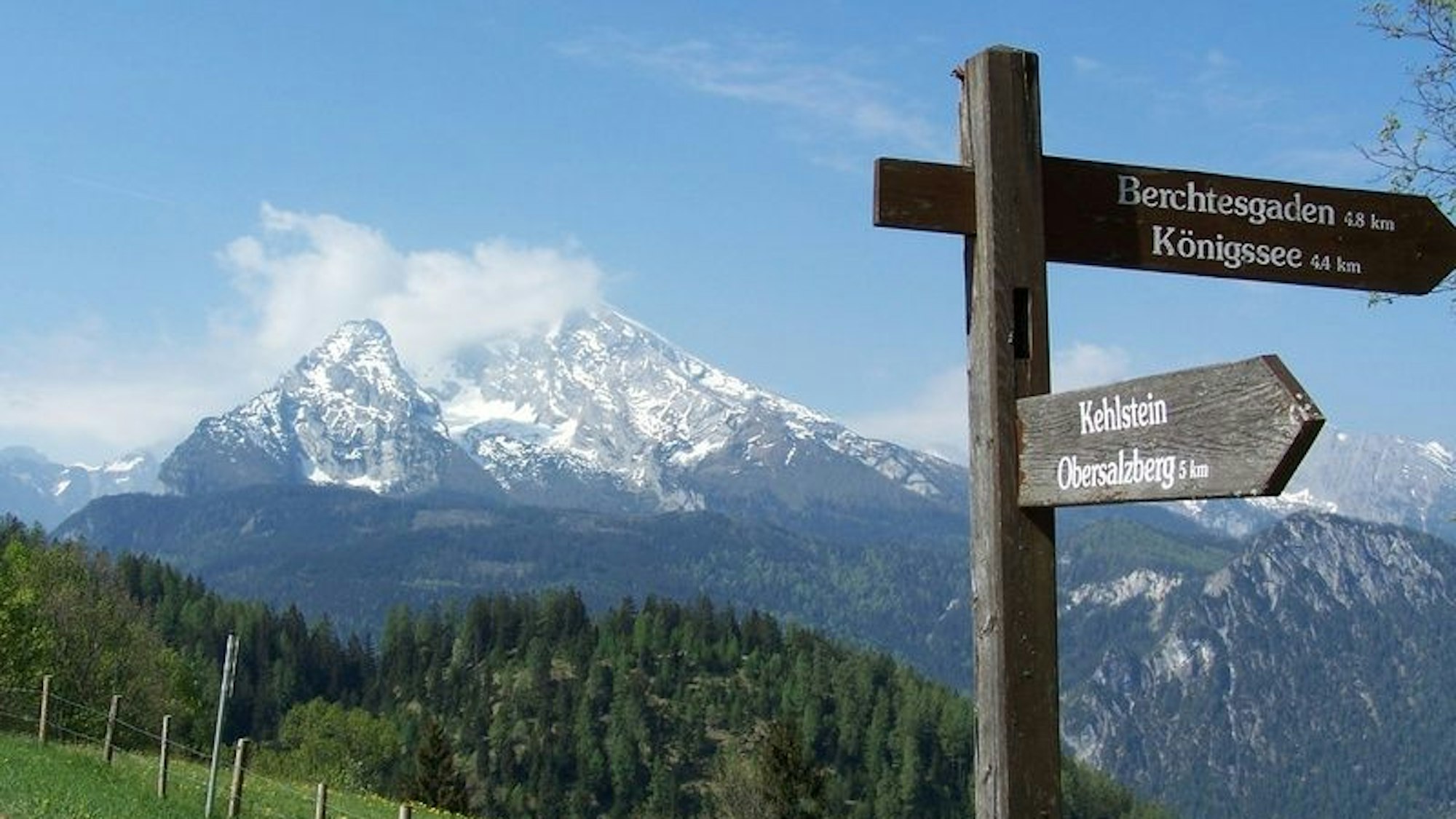 Ein Wegweiser steht vor den Berchtesgadener Alpen.