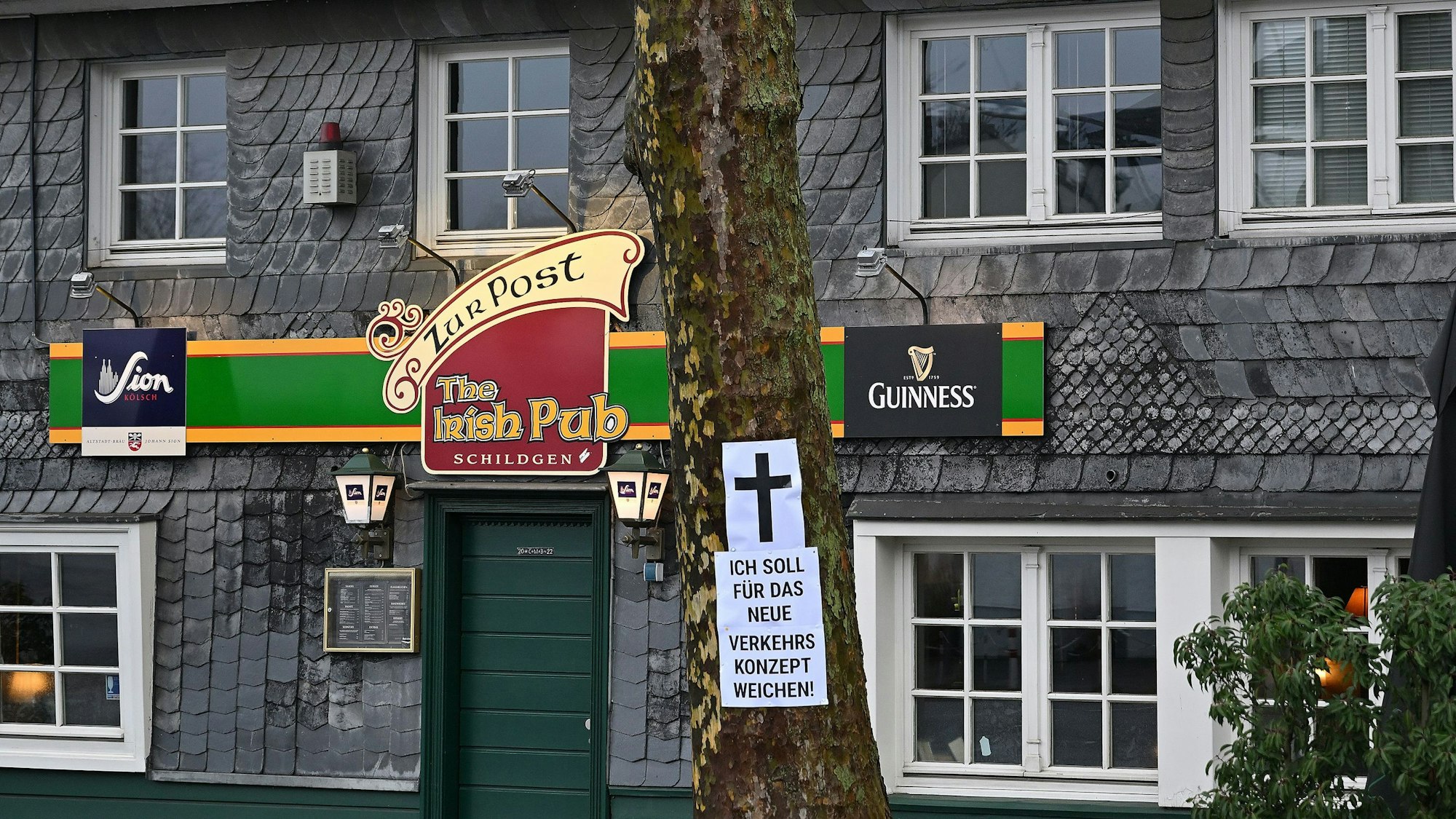 Zu sehen ist die Fassade aus Schiefer der Gaststätte mit dem Baum davor.