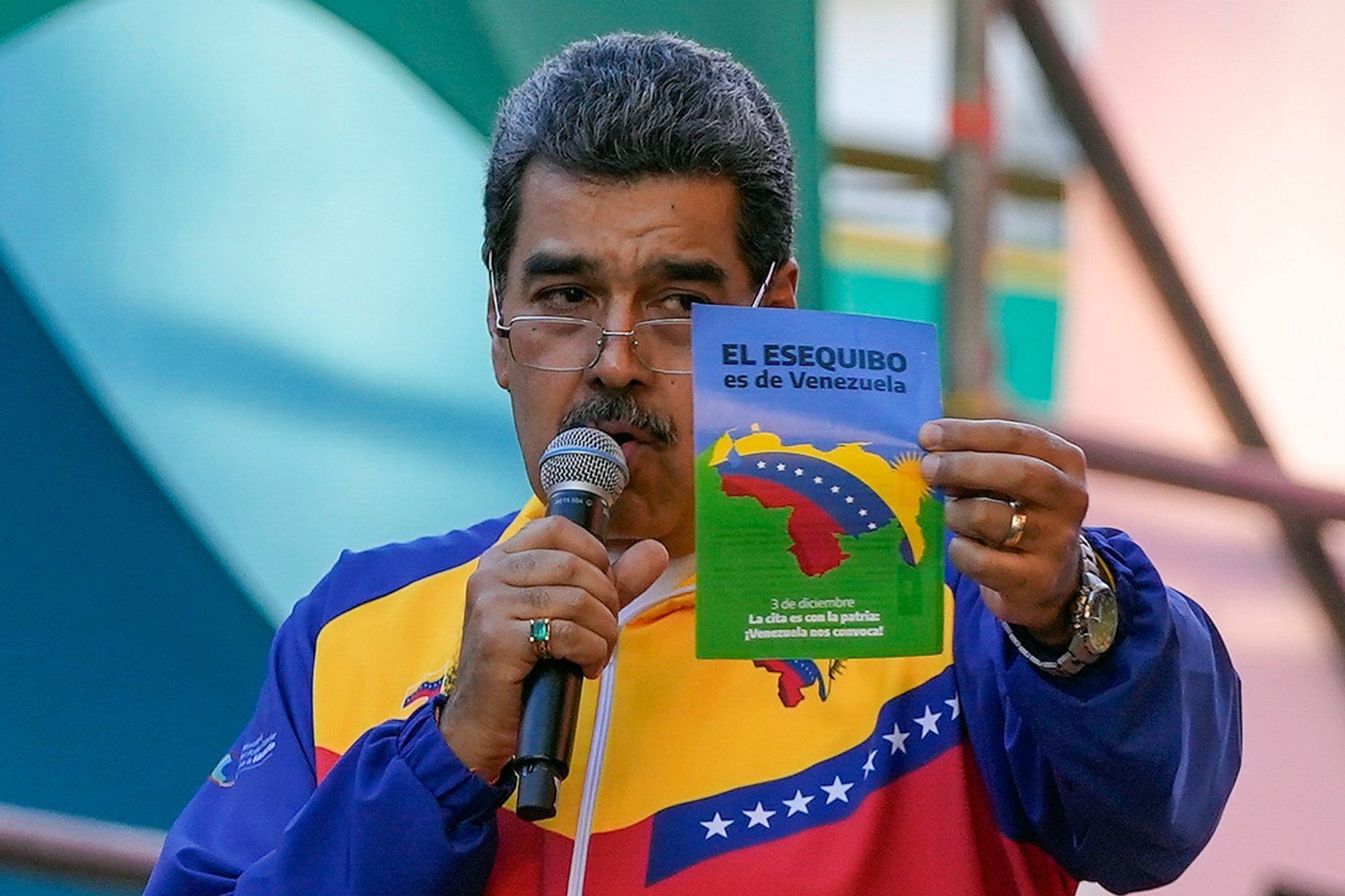 Venezuelas Präsident Nicolás Madurospricht in ein Mikrofon, während er einen Flyer hochhält.