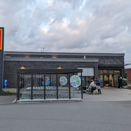 Ein Aldi-Markt mit Klinkerfassade, Unterstellplatz für Einkaufswagen und einer großen Stele mit Aldi-Schild.