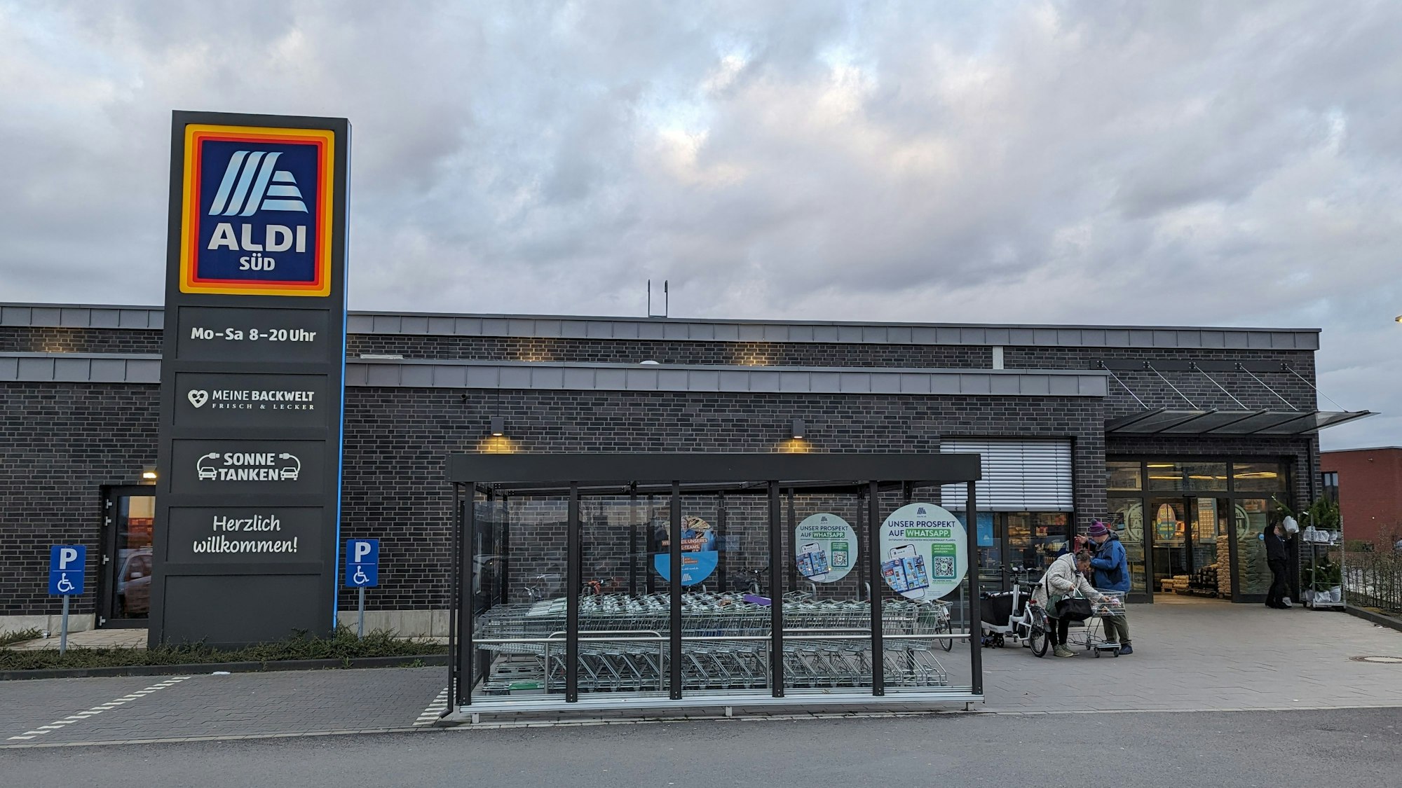Ein Aldi-Markt mit Klinkerfassade, Unterstellplatz für Einkaufswagen und einer großen Stele mit Aldi-Schild.