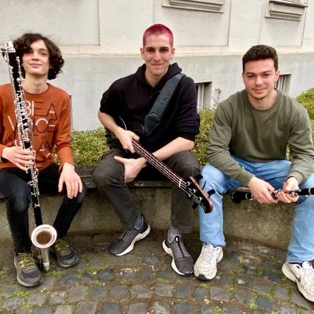 Zu sehen sind drei junge Musiker mit ihren Instrumenten.