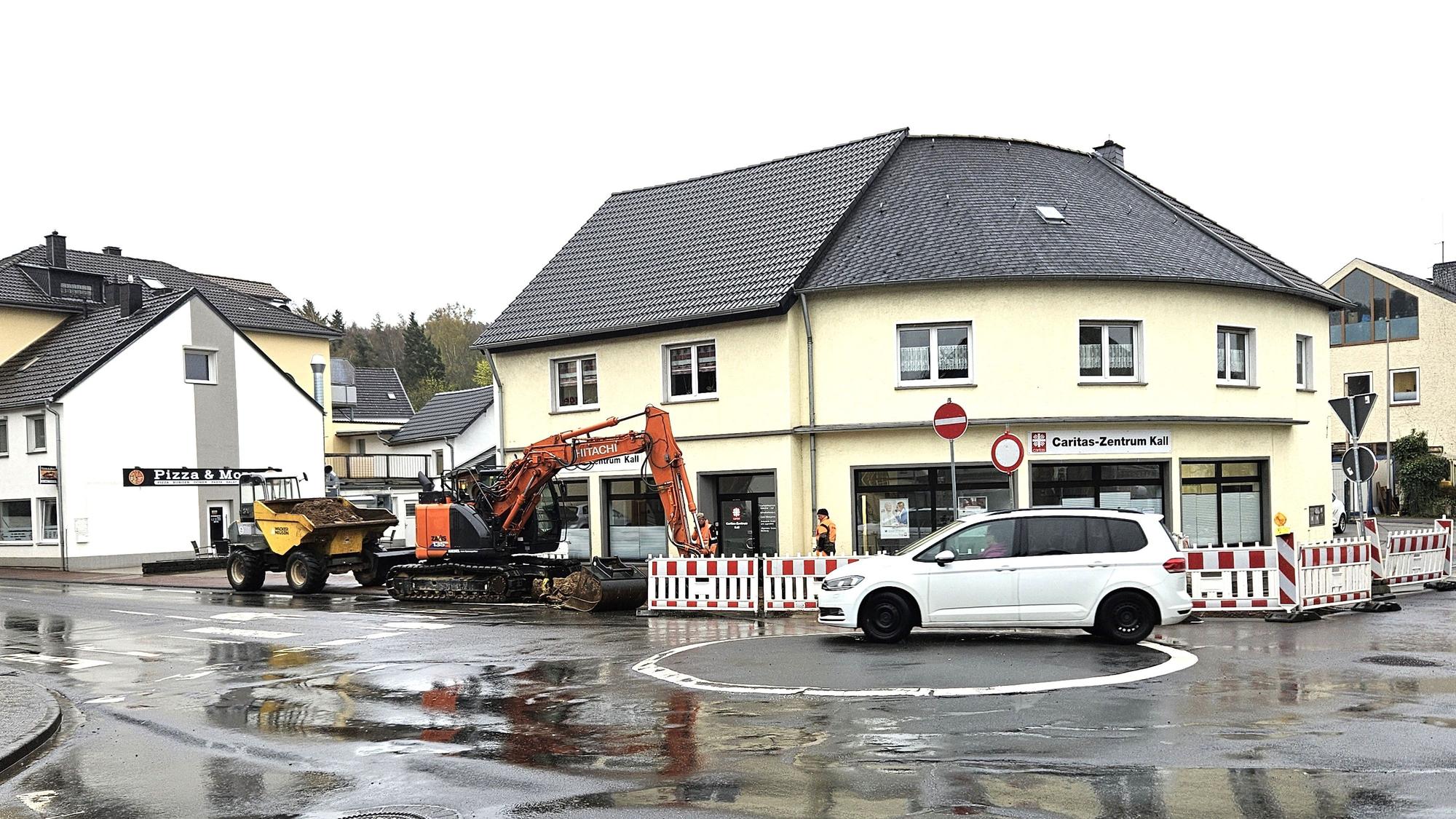 Ein Bagger ist am Kreisverkehr Aachener Straße/Bahnhofstraße im Einsatz. Ein weißes Auto fährt an der Baustelle vorbei.