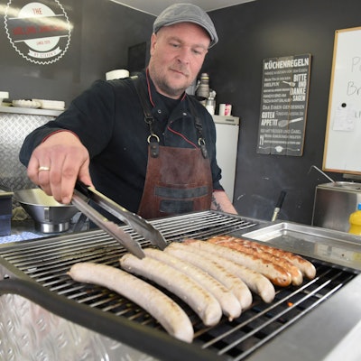 Der gelernte Metzger legt Würste auf den Grill.