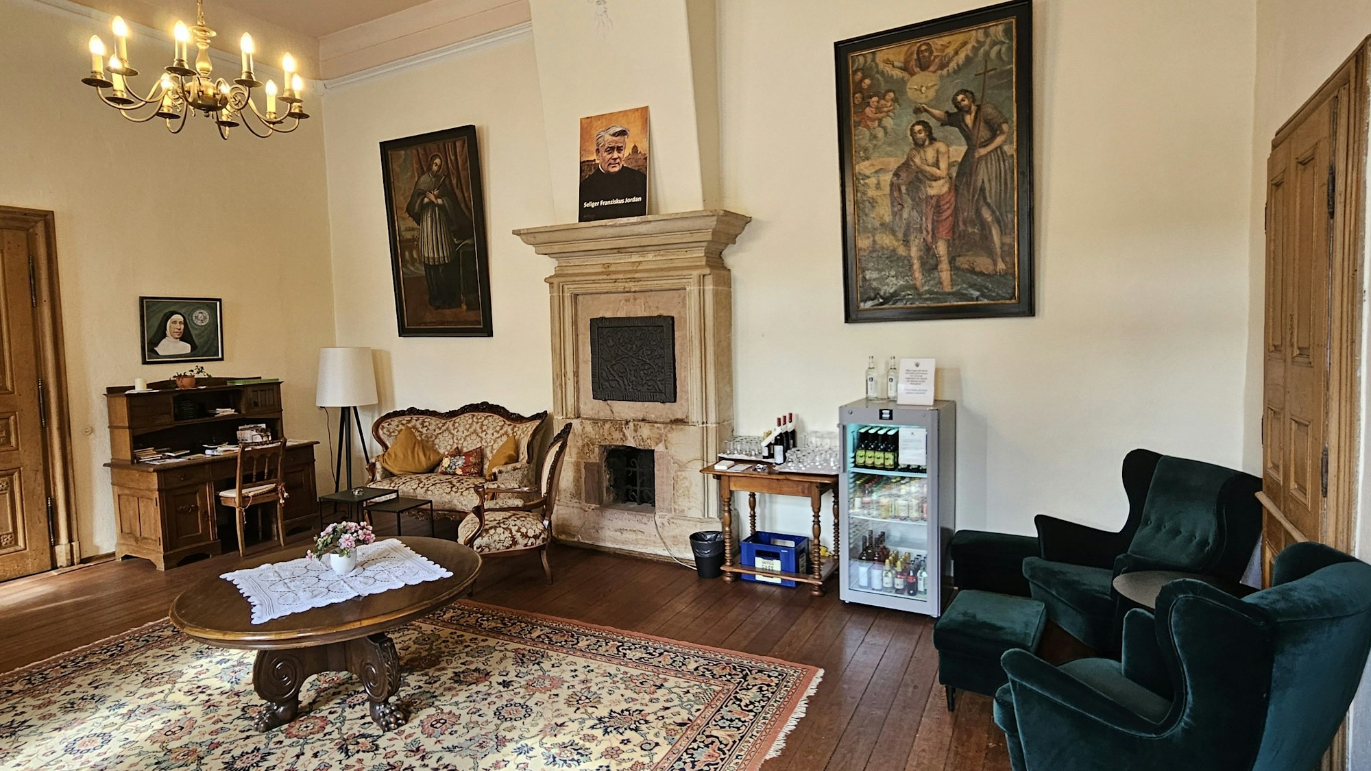 Blick in ein Zimmer mit Kamin, Holztisch und verschiedenen Sitzmöglichkeiten.