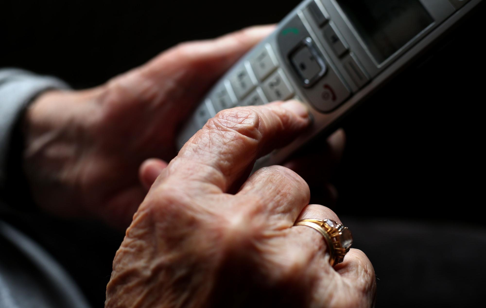 Eine ältere Frau tippt auf einem schnurlosen Festnetztelefon.