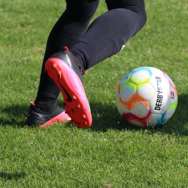 Die Füße eines Fußballspielers in pink-schwarzen Schuhen sind zu sehen, kurz bevor er einen Ball schießt.