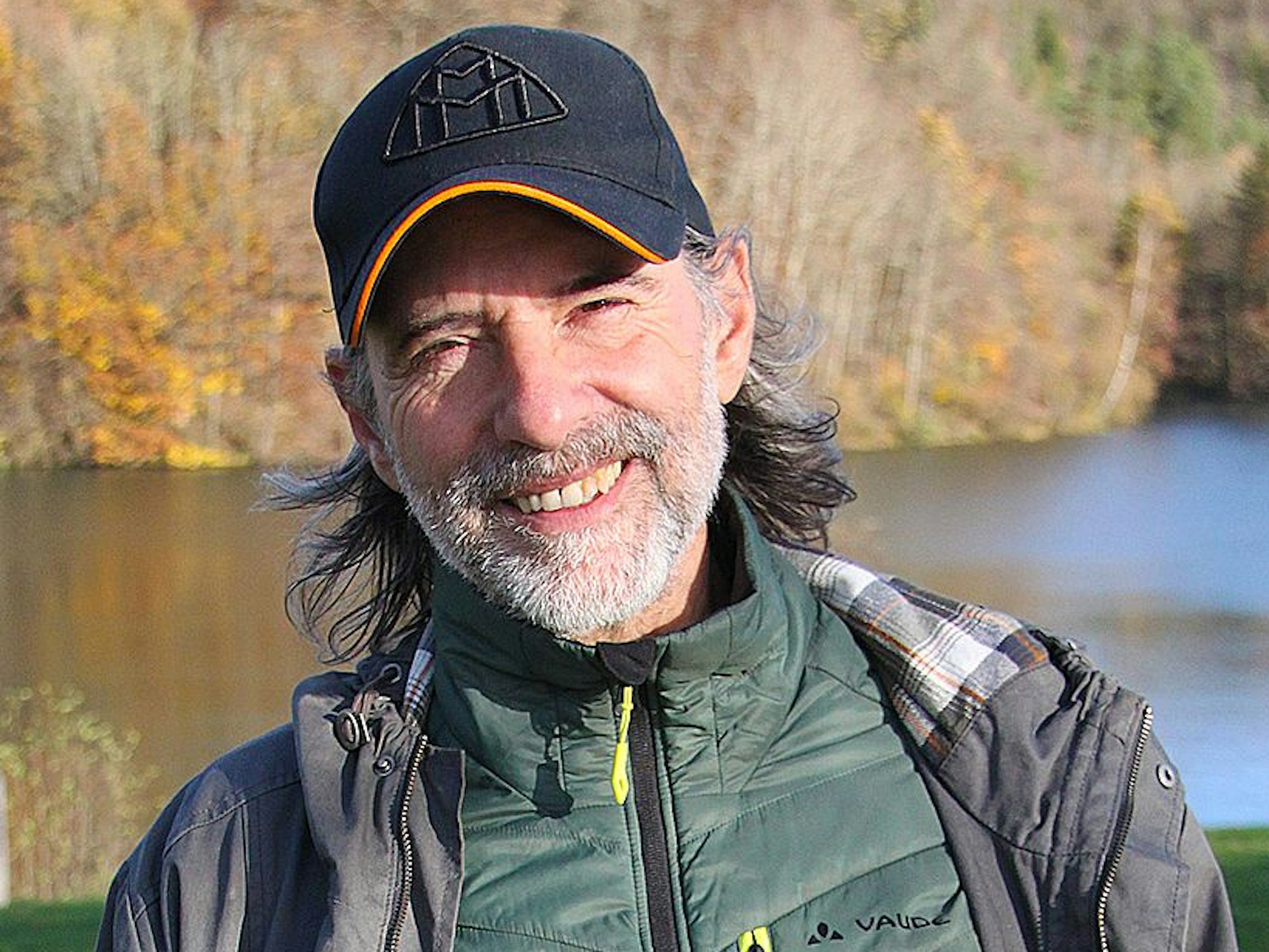 Ein Mann mit Bart und Kappe, dahinter ein See.