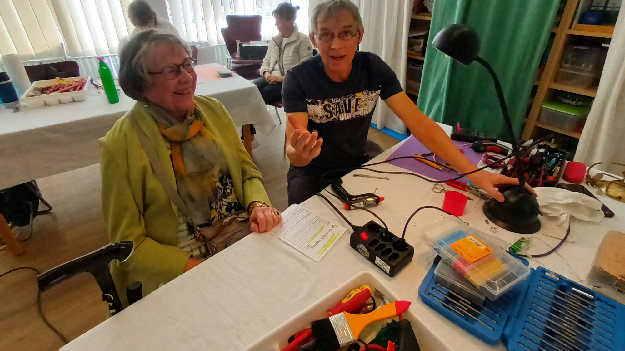 Eine Mann und eine Frau an einem Tisch, darauf Werkzeuge und eine Lampe