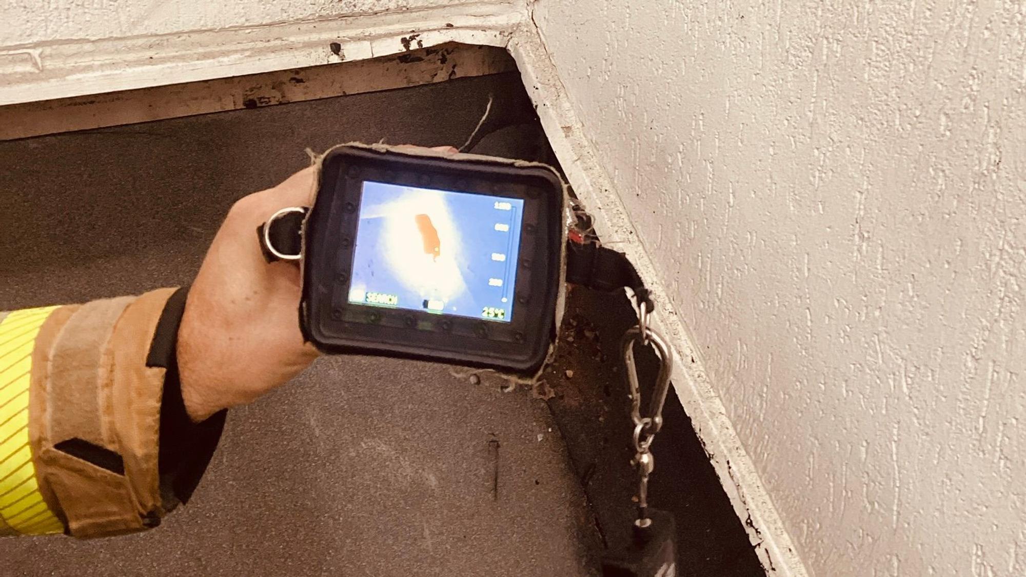 Ein Feuerwehrmann hält eine Wärmekamera auf den Abschluss eines frisch mit Dachpappe verschweißten Daches, unter dem offenbar ein Schwelbrand ausgebrochen ist.