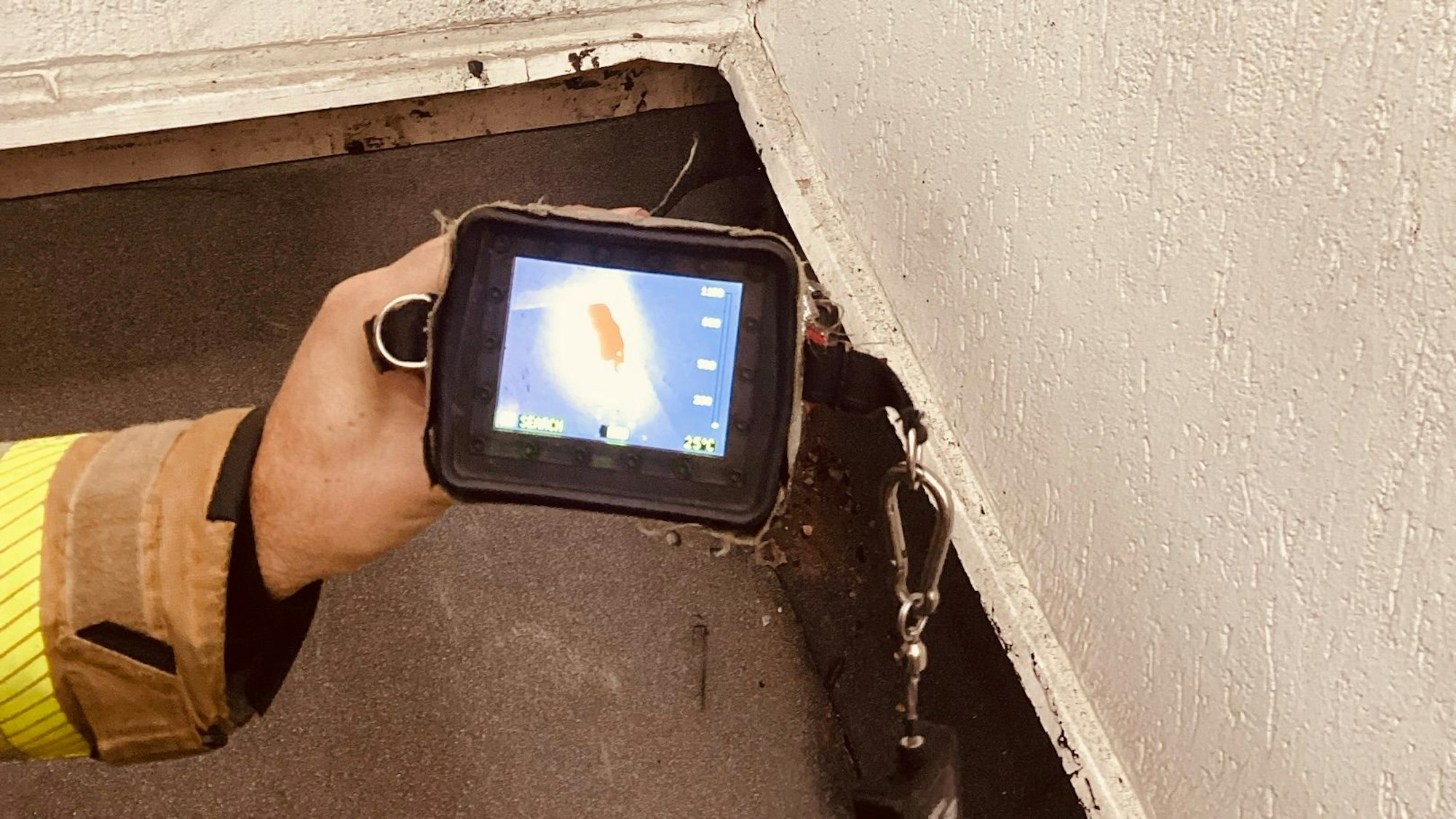 Ein Feuerwehrmann hält eine Wärmekamera auf den Abschluss eines frisch mit Dachpappe verschweißten Daches, unter dem offenbar ein Schwelbrand ausgebrochen ist.