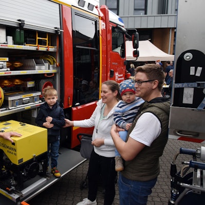Ein Feuerwehrmann erläutert einer jungen Familie die Ladung eines Feuerwehrautos.