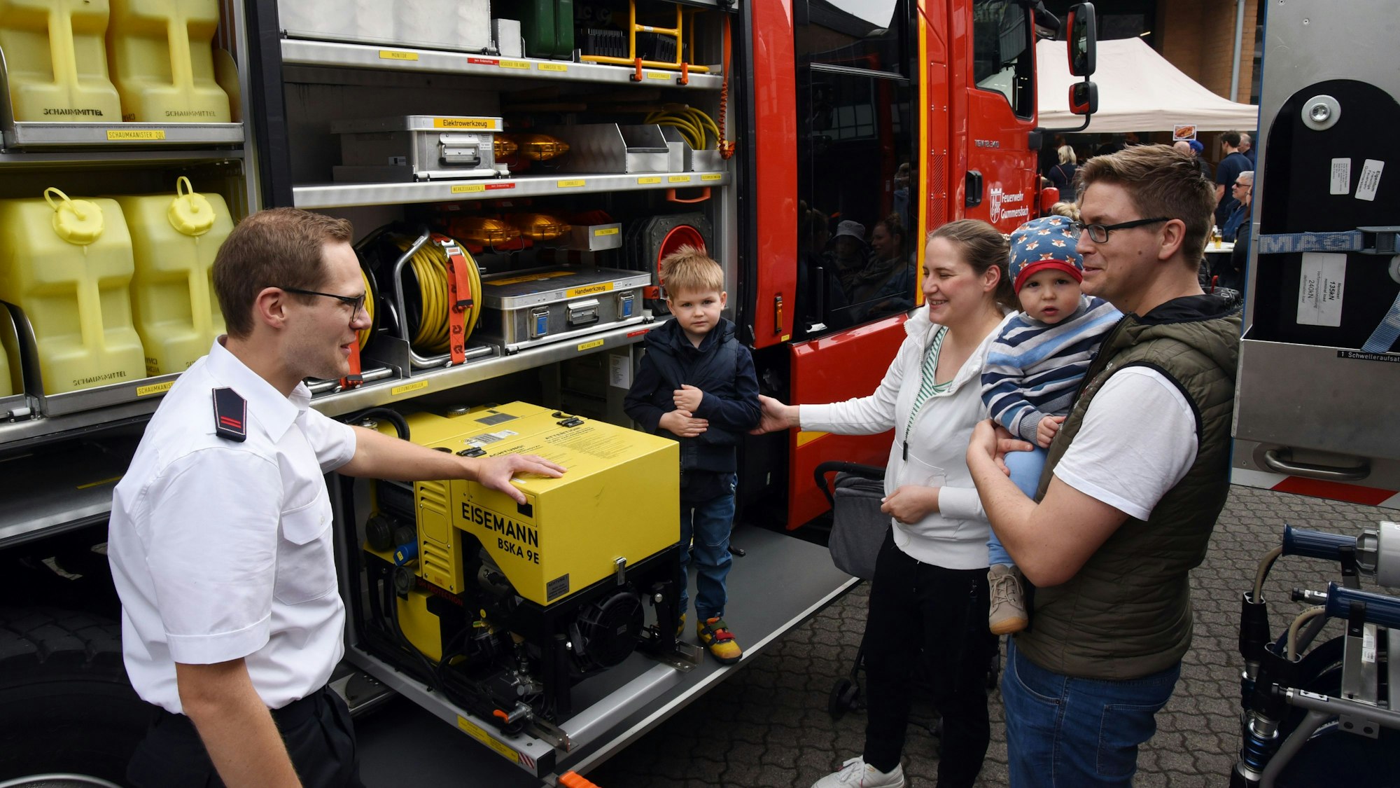 Ein Feuerwehrmann erläutert einer jungen Familie die Ladung eines Feuerwehrautos.