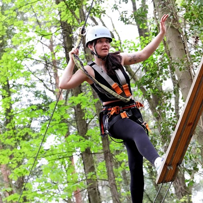 Zu sehen ist eine junge Frau, die gut gesichert über eine Planke balanciert.