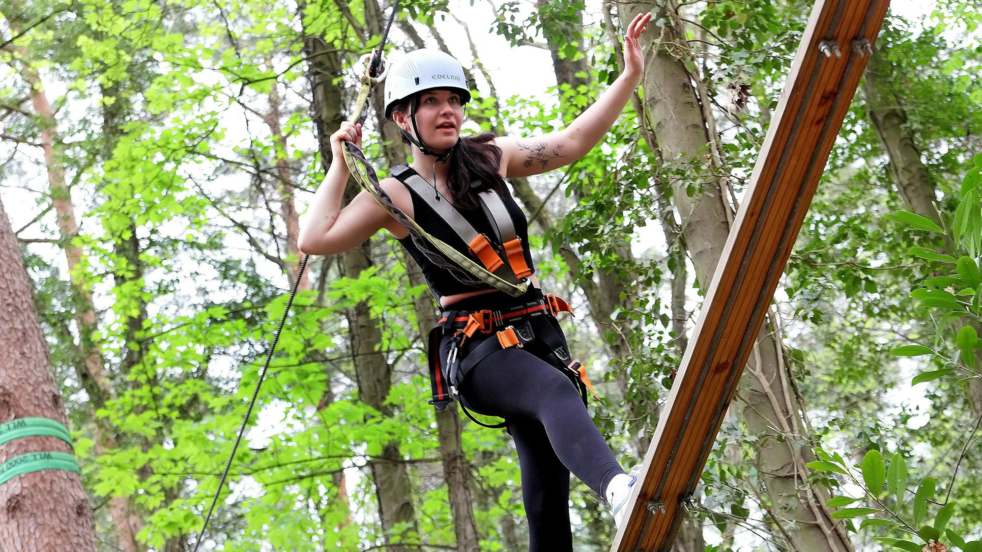 Zu sehen ist eine junge Frau, die gut gesichert über eine Planke balanciert.