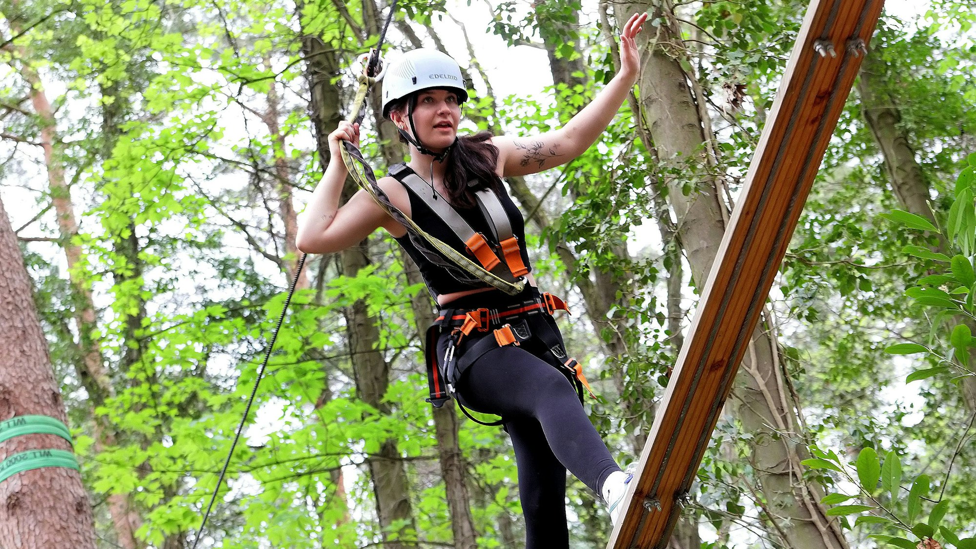 Zu sehen ist eine junge Frau, die gut gesichert über eine Planke balanciert.