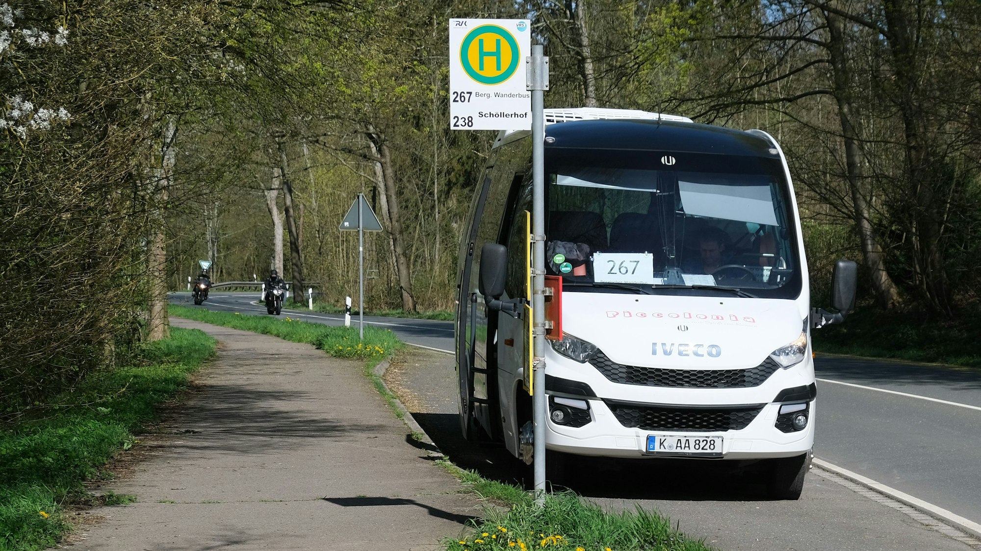 Zu sehen ist ein Bus an einer Bushaltestelle am Straßenrand.