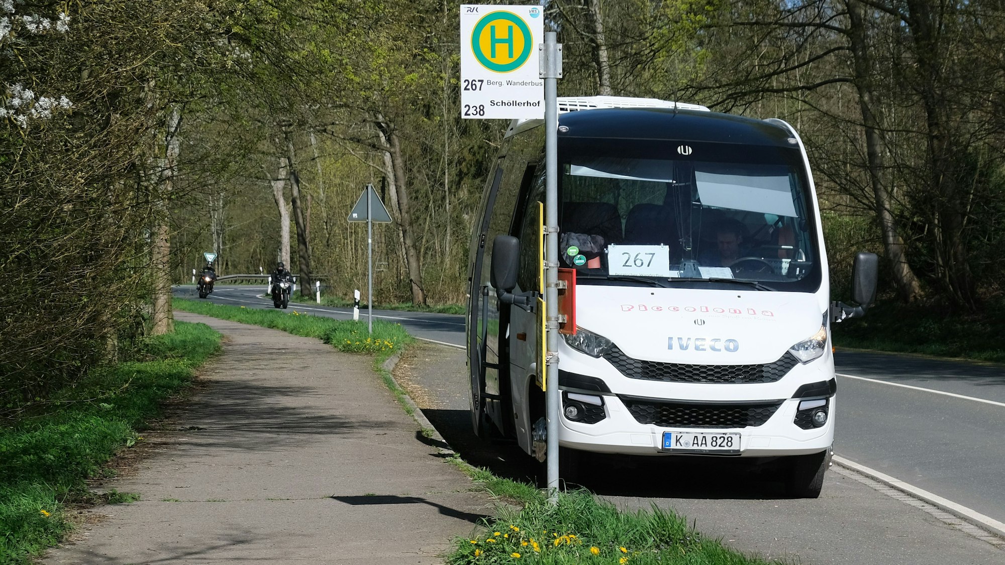 Der weiße Kleinbus steht an einer Haltestelle an einer Landstraße.