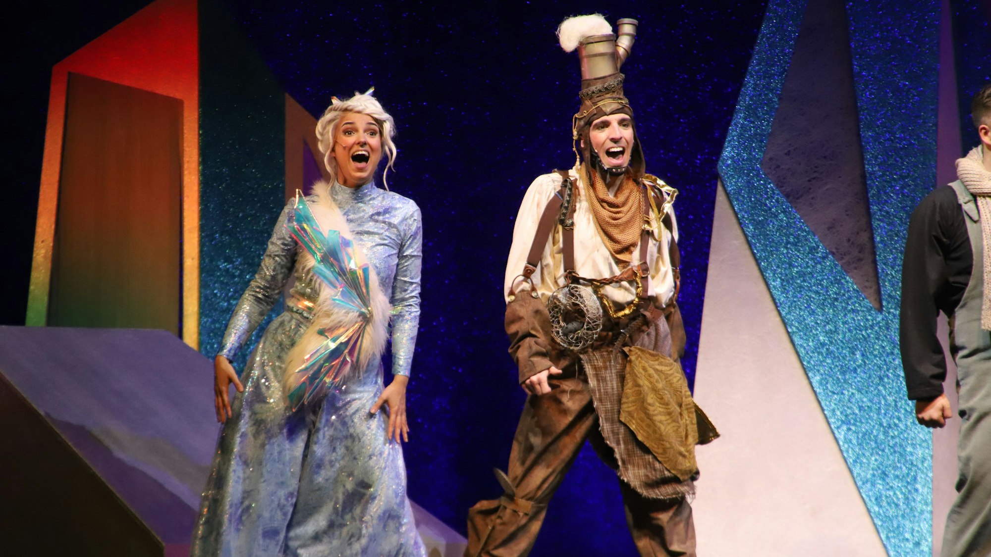 Eine Frau und ein Mann im Kostüm singen auf einer bunt beleuchteten Bühne.