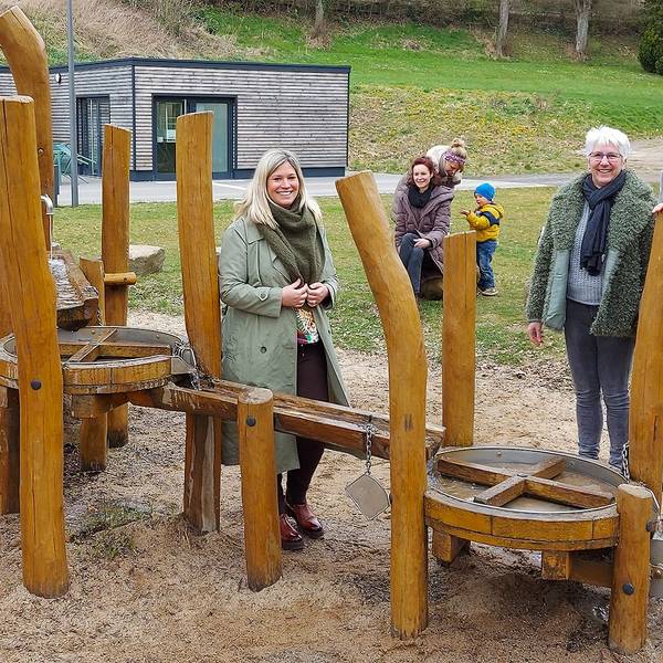 Bürgermeisterin Jennifer Meuren, Annegret Dreimüller und Guido Waters stehen am Kleinkinderspielplatz. Einige Kinder spielen.