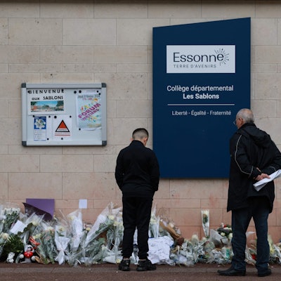 Anwohner betrachten die Blumen, die vor dem Eingang der Mittelschule Les Sablons in Viry-Chatillon niedergelegt worden sind.
