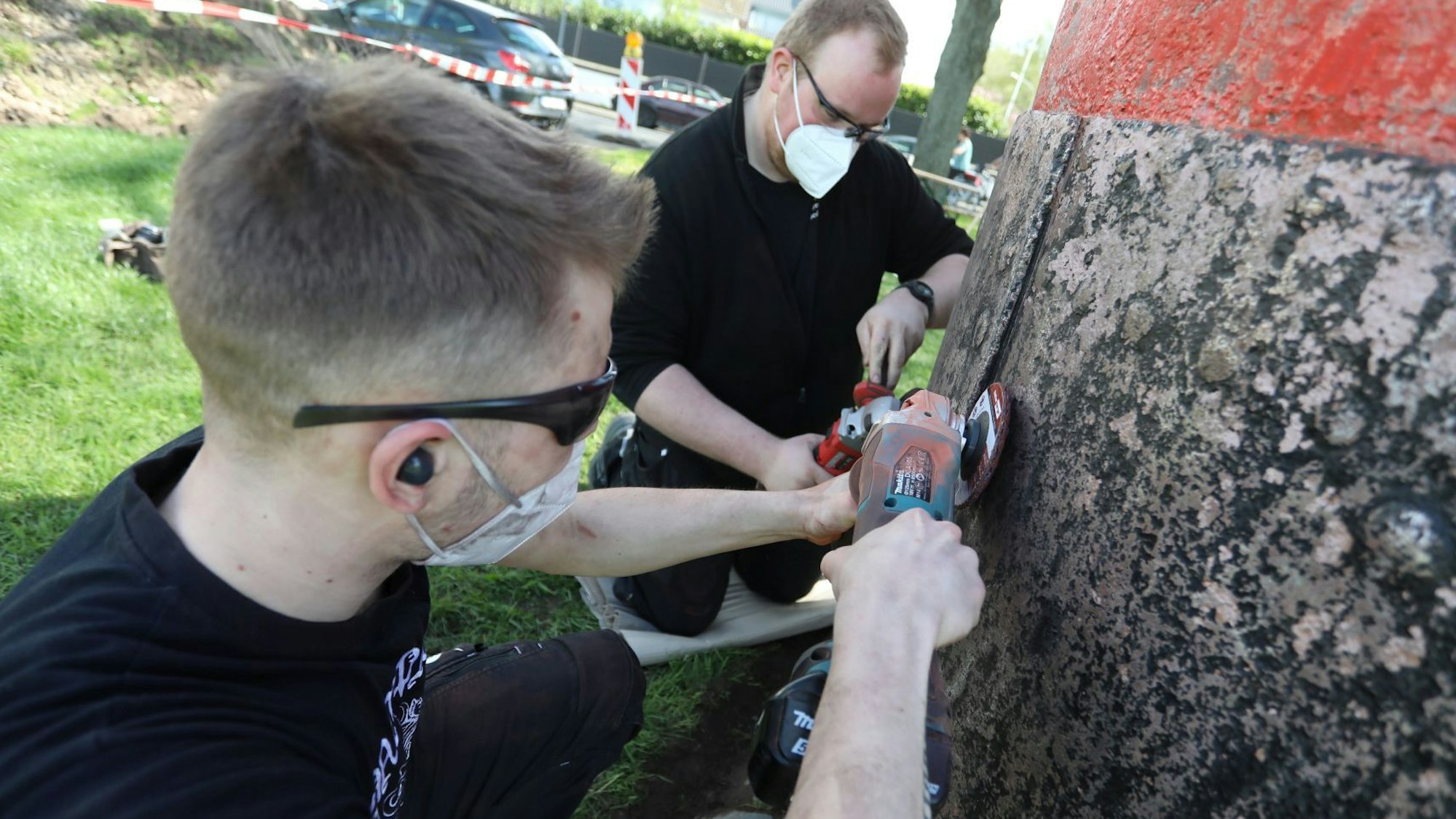 Zwei Männer mit Mundschutz und Brille flexen rostige Stellen der schwarz-roten Boje.