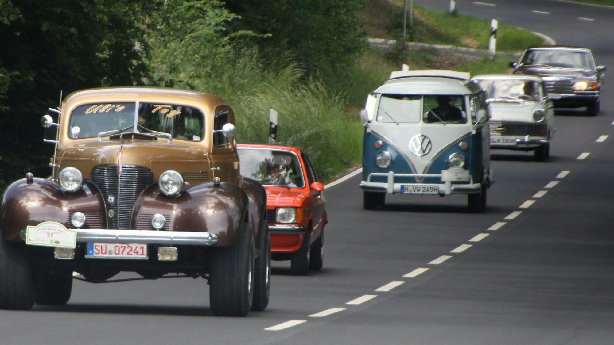 Fünf Oldtimer fahren hintereinander auf einer Straße.
