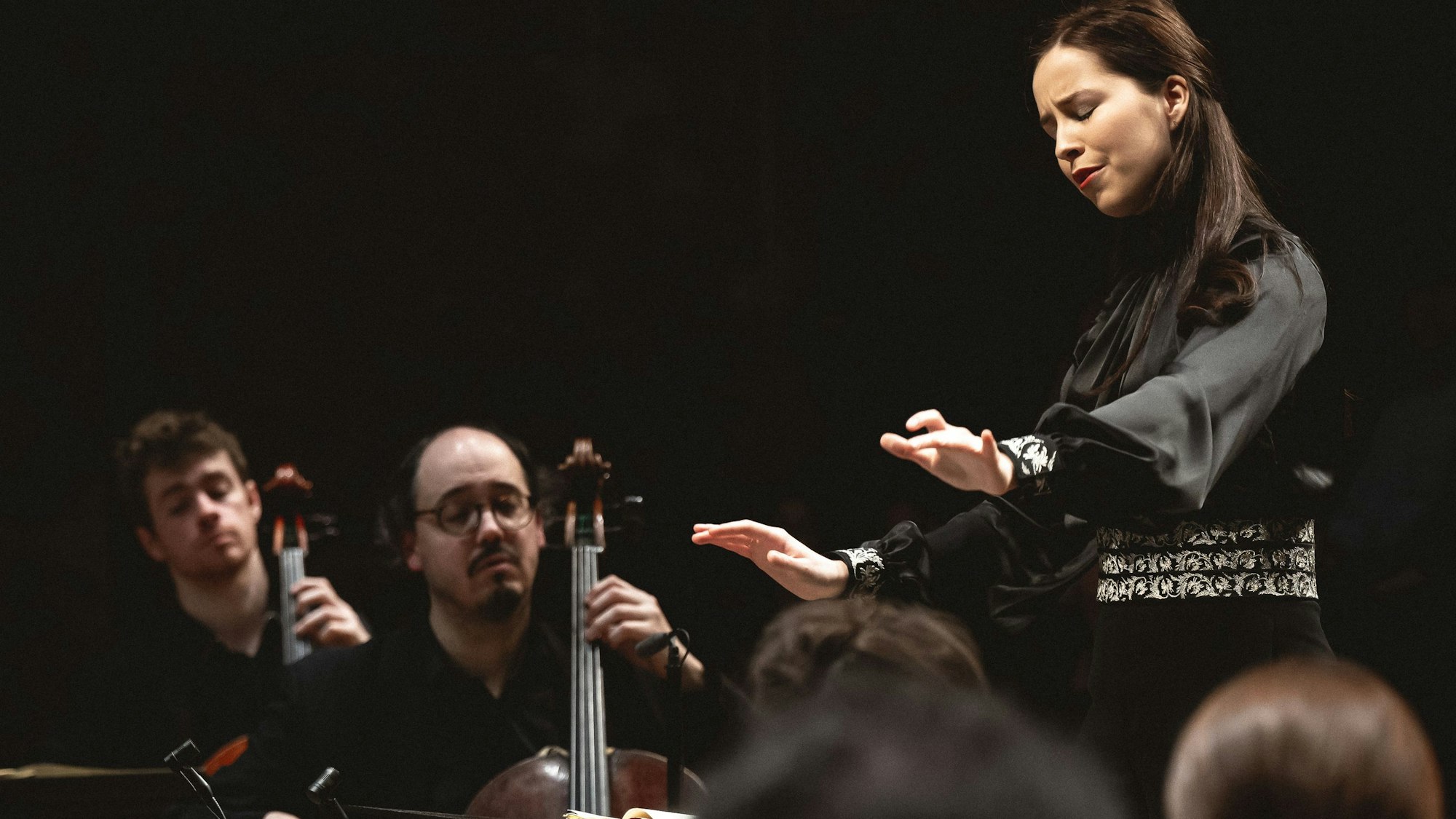 Auf dem Bild ist eine junge Dirigentin mit Musikern zu sehen.