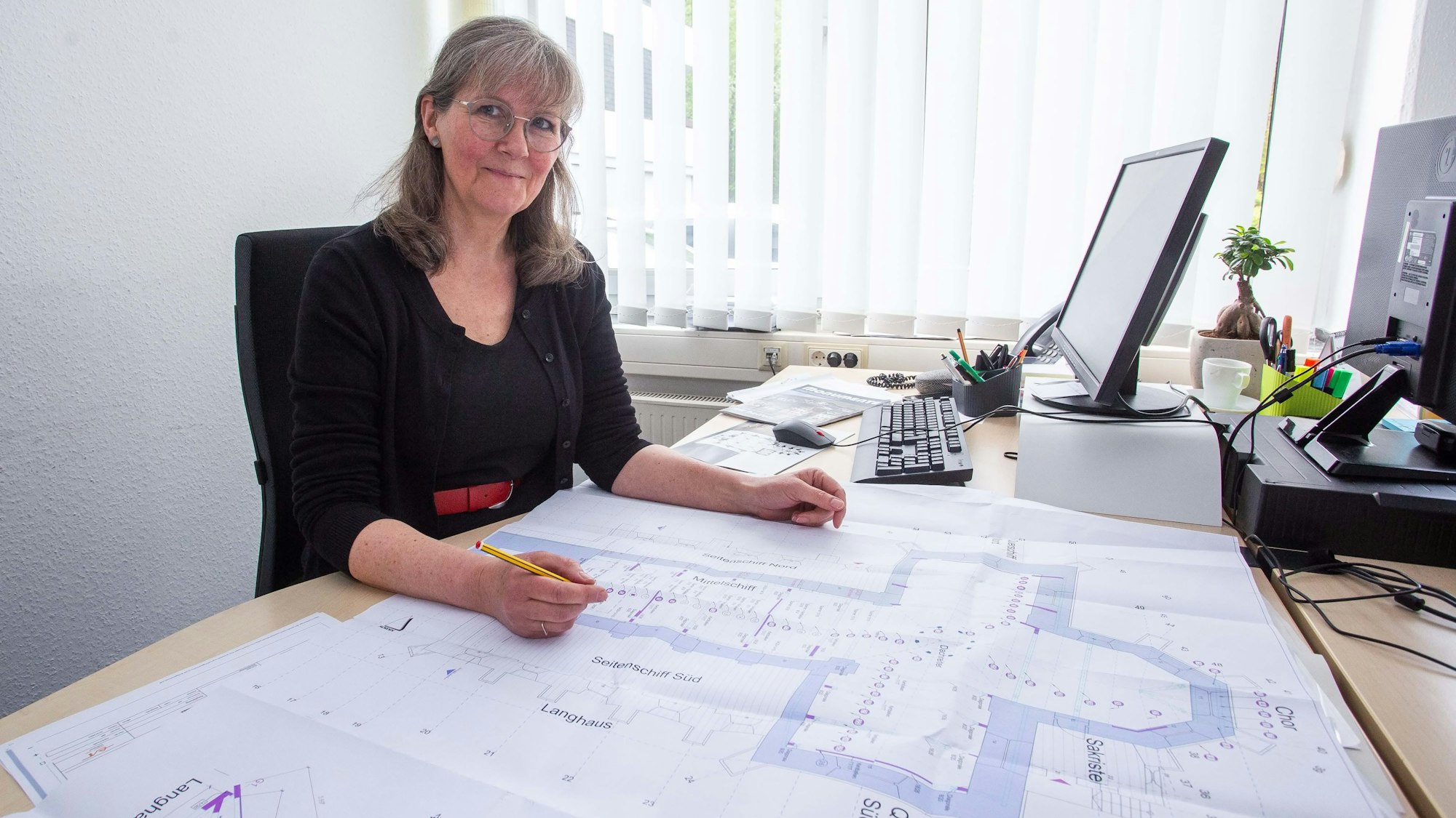 Eine Frau sitzt am Tisch vor einer Planzeichnung.
