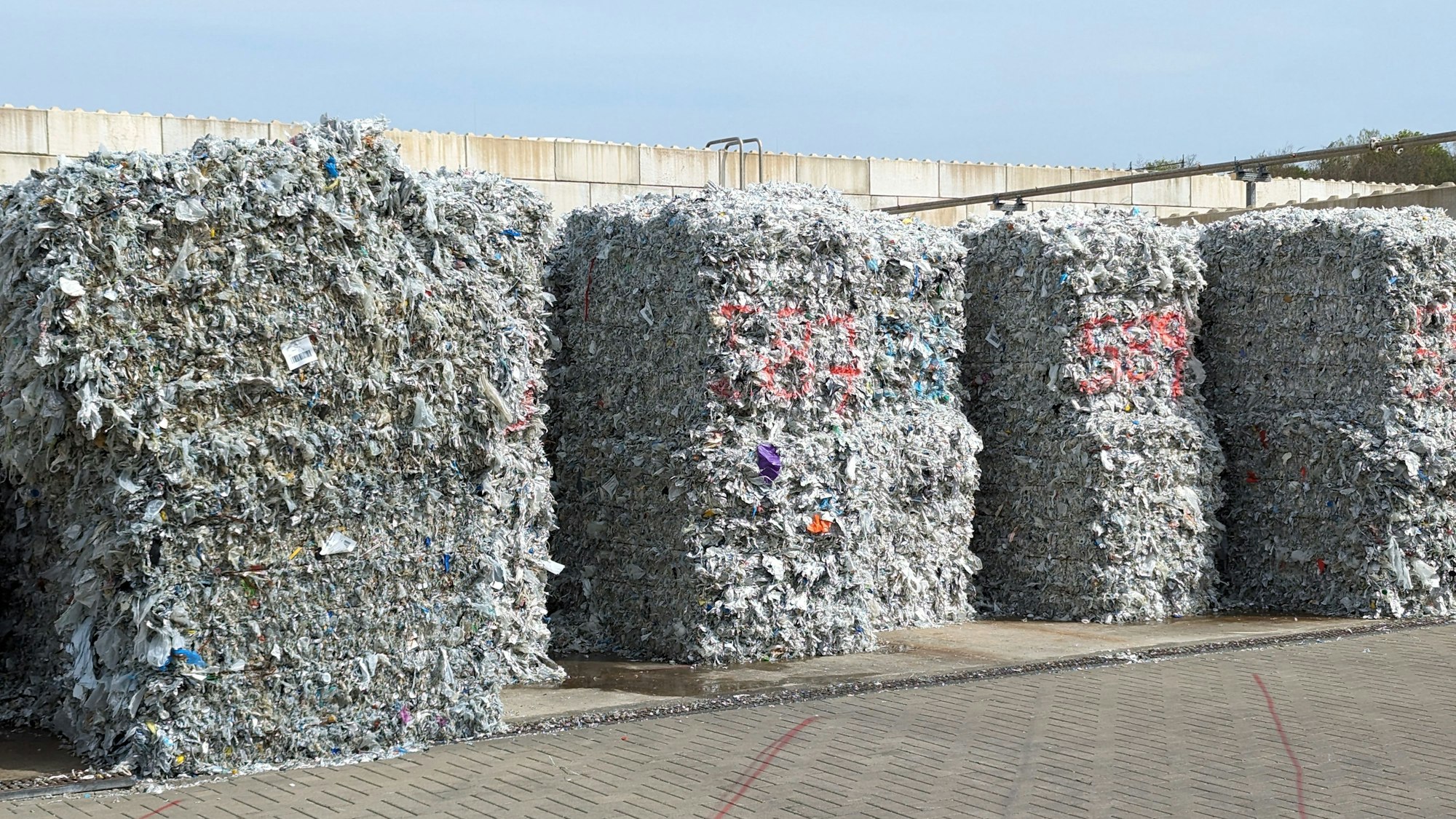 Auf einer betonierten Fläche lagern große Ballen mit gepresstem Material.