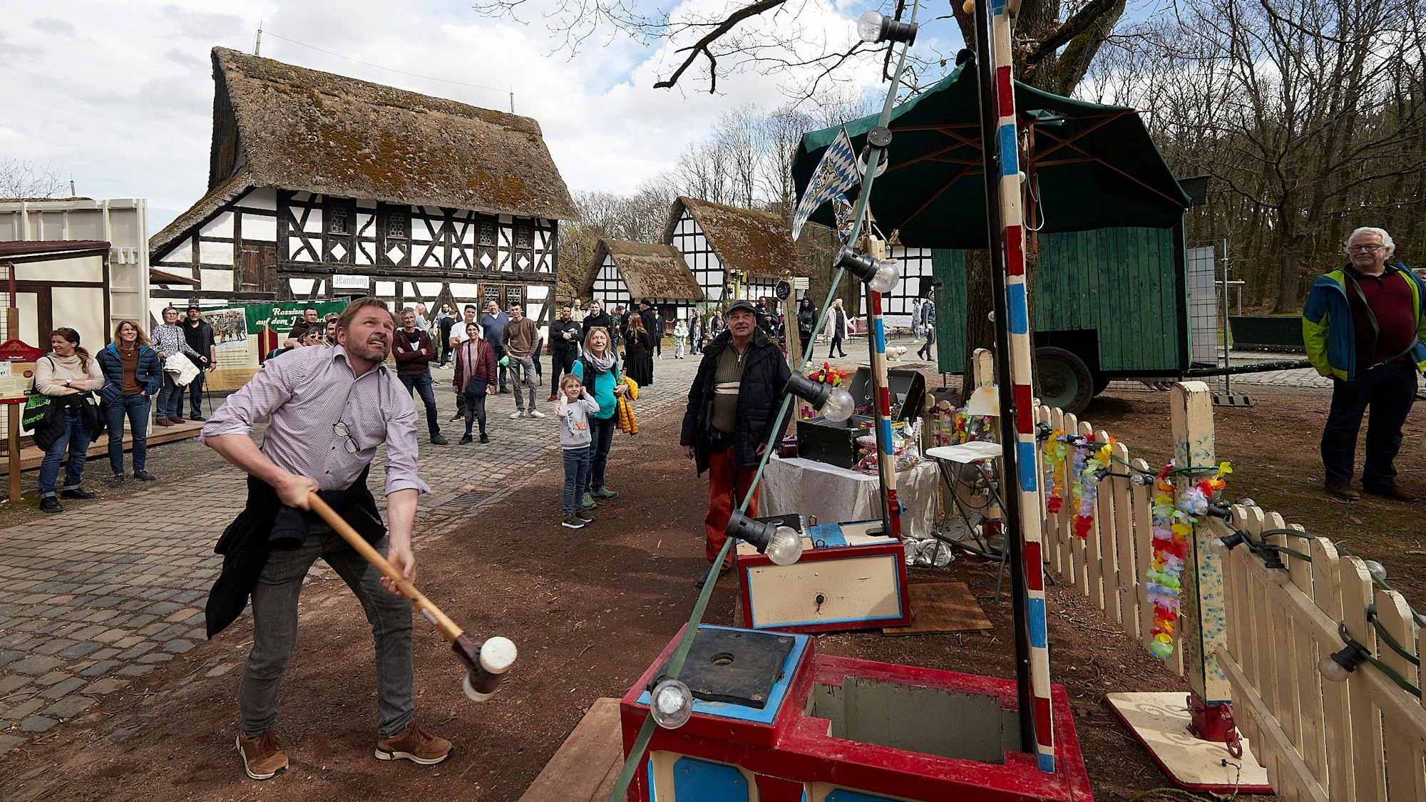 Ein Besucher des historischen Jahrmarkts schwingt den Hammer beim „Hau den Lukas“. Im Hintergrund stehen Fachwerkhäuser.