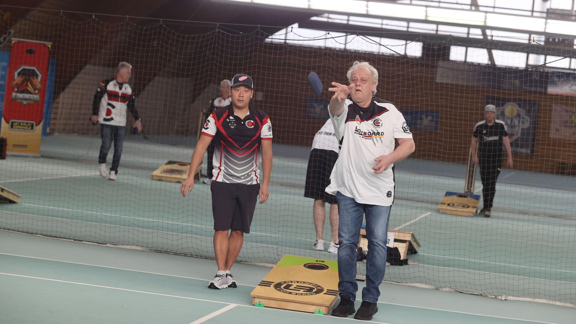 Spielszene aus dem Trendsport Cornhole, ein Mann wirft ein mit Granulat gefülltes Säckchen