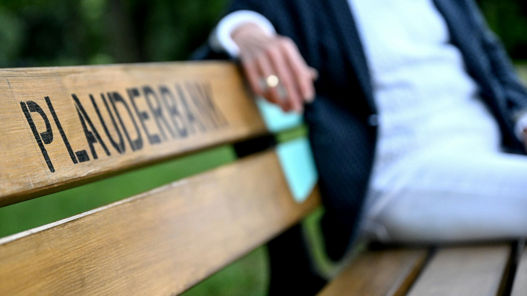 Auf einer Holzbank mit der Aufschrift in schwarzen Druckbuchstaben sitzt jemand.