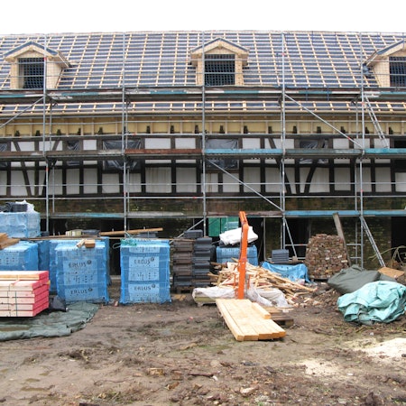 Ein langgestrecktes Fachwerkgebäude ist eingerüstet, das Dach ist für die Neueindeckung vorbereitet.